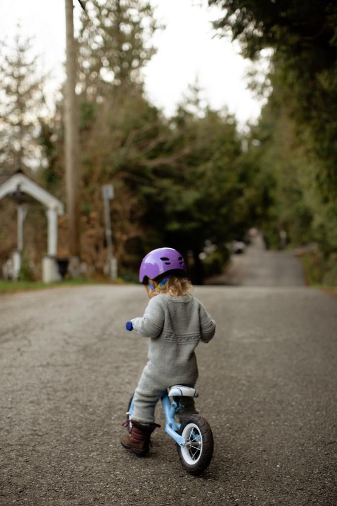 copil blond cu casca mov ce merge pe o bicicleta albastra fara pedale 